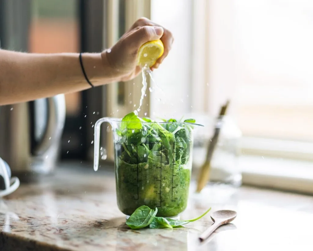Main pressant un citron au-dessus d'un verre doseur rempli d'épinards