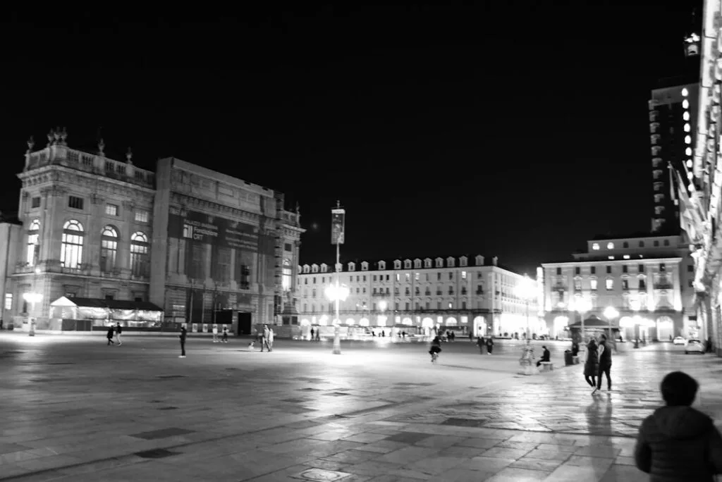 Place illuminée la nuit à Turin avec quelques passants et lampadaires